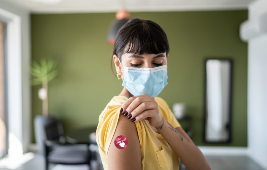 Young woman wearing protective face mask showing arm with 'Got vaccinated' sticker on at MD Now
